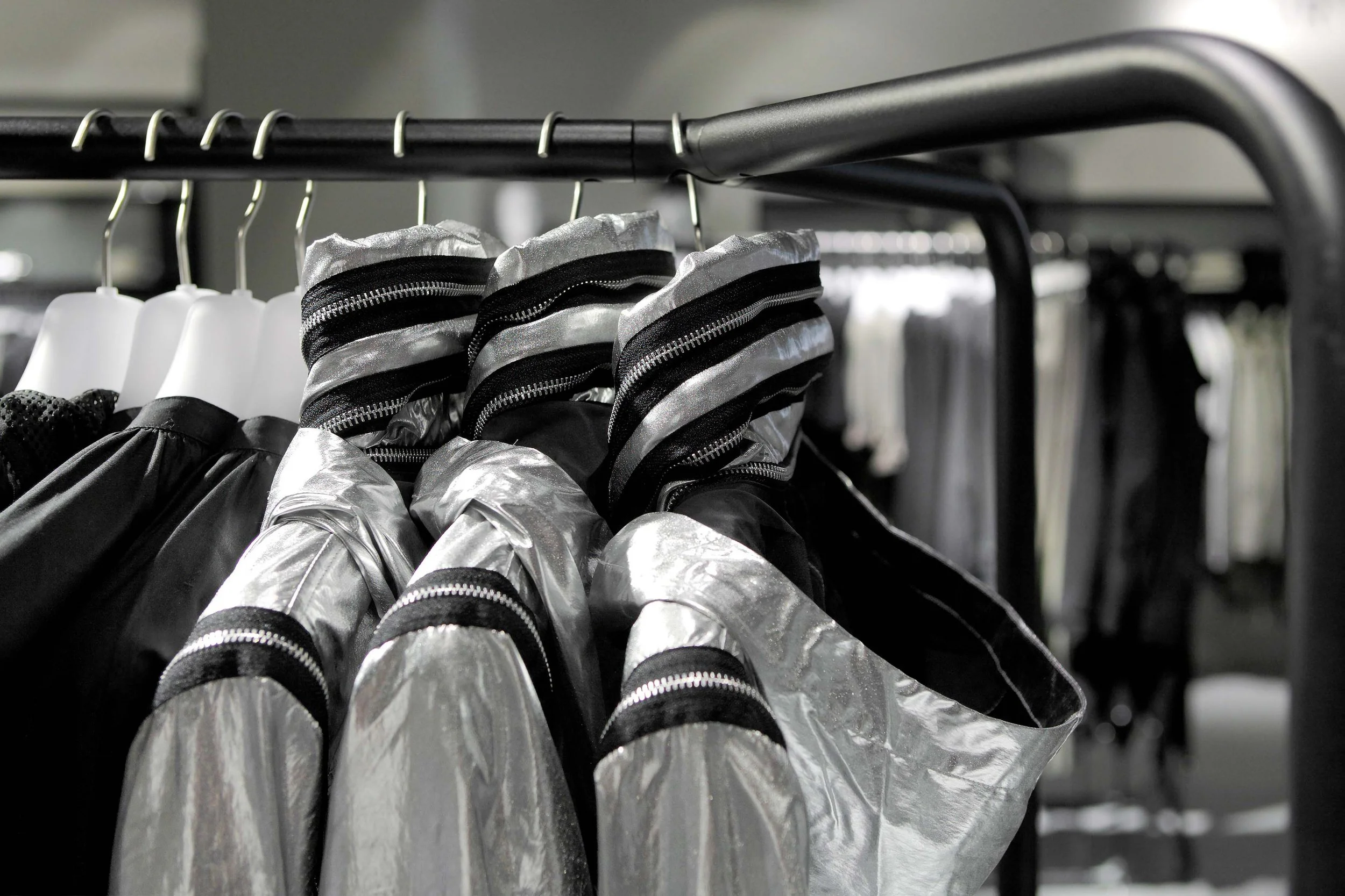 Black and silver jackets or coats hanging on black hangers on a metal clothing rack.