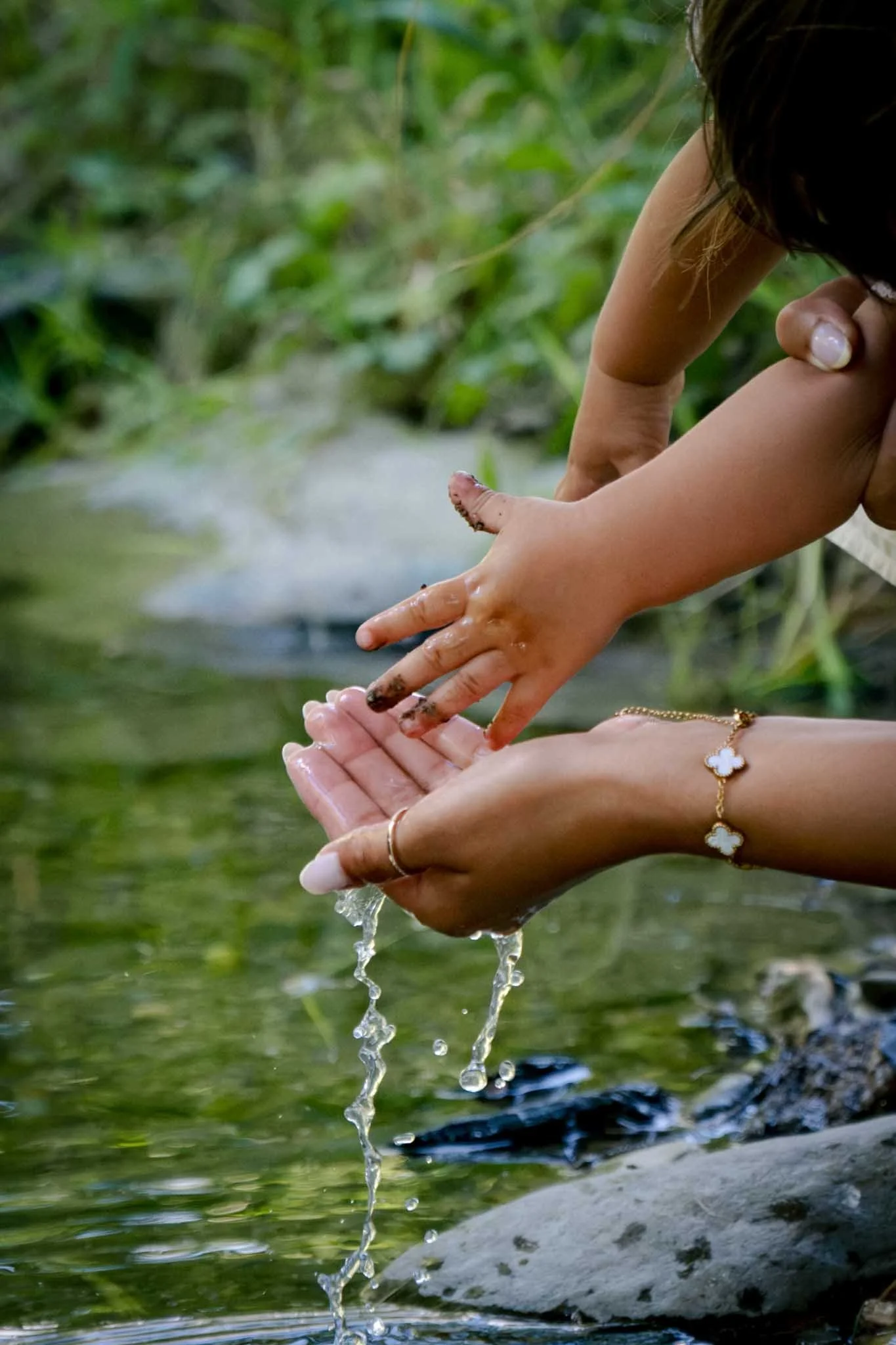Hände eines Mädchens, das Wasser in einem Fluss an den Händen sammelt, mit einer Kette mit Kleeblatt-Anhänger um den Hals sichtbar. Entstanden bei einem Familien Shooting in Schmitten im Taunus.