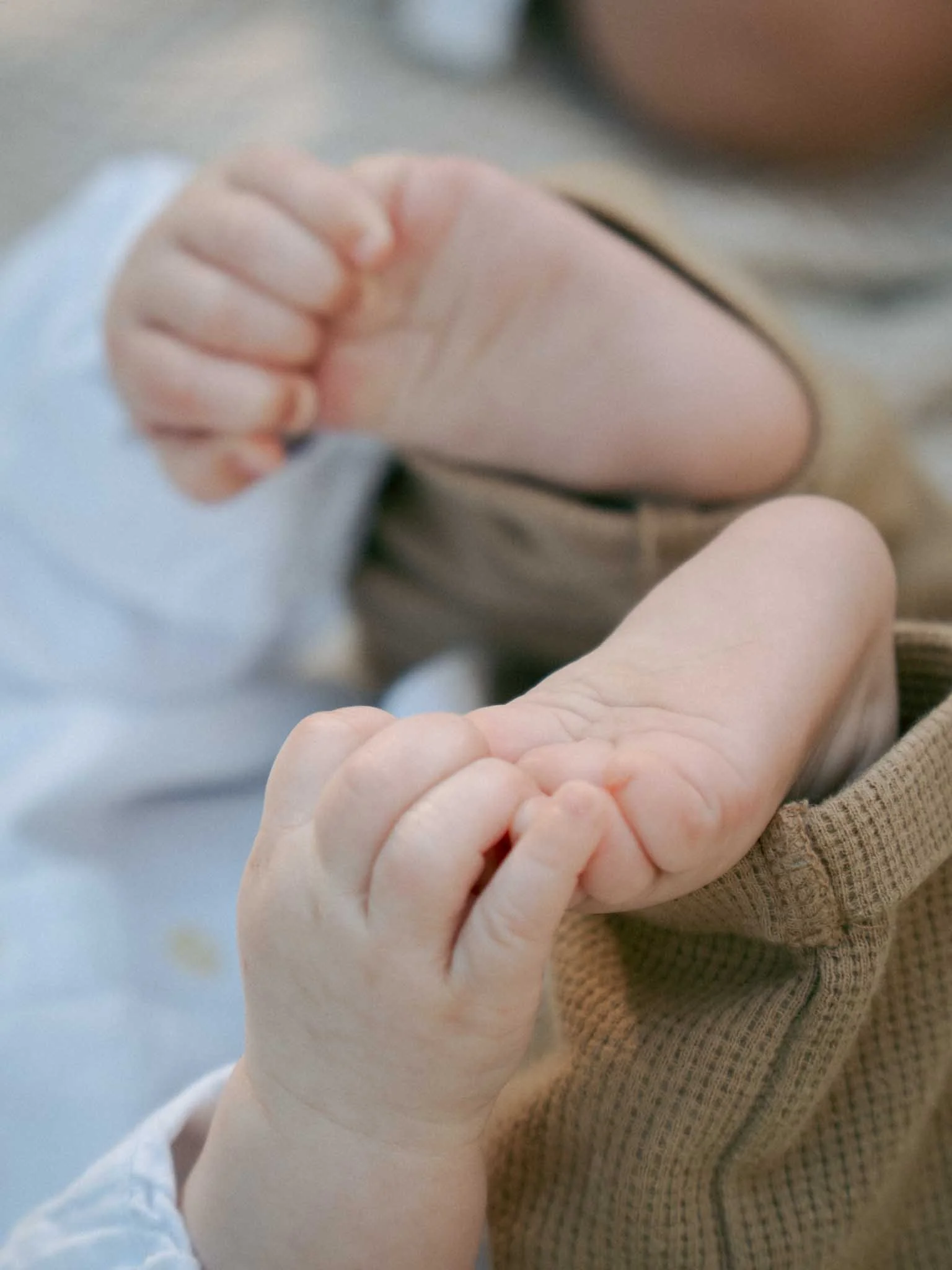 Eine Nahaufnahme einer menschlichen Hand, die eine kleine Babyhand hält, mit einer Person im Hintergrund, die eine weitere Hand ausstreckt. Entstanden bei einem Familien Shooting in Schmitten im Taunus.