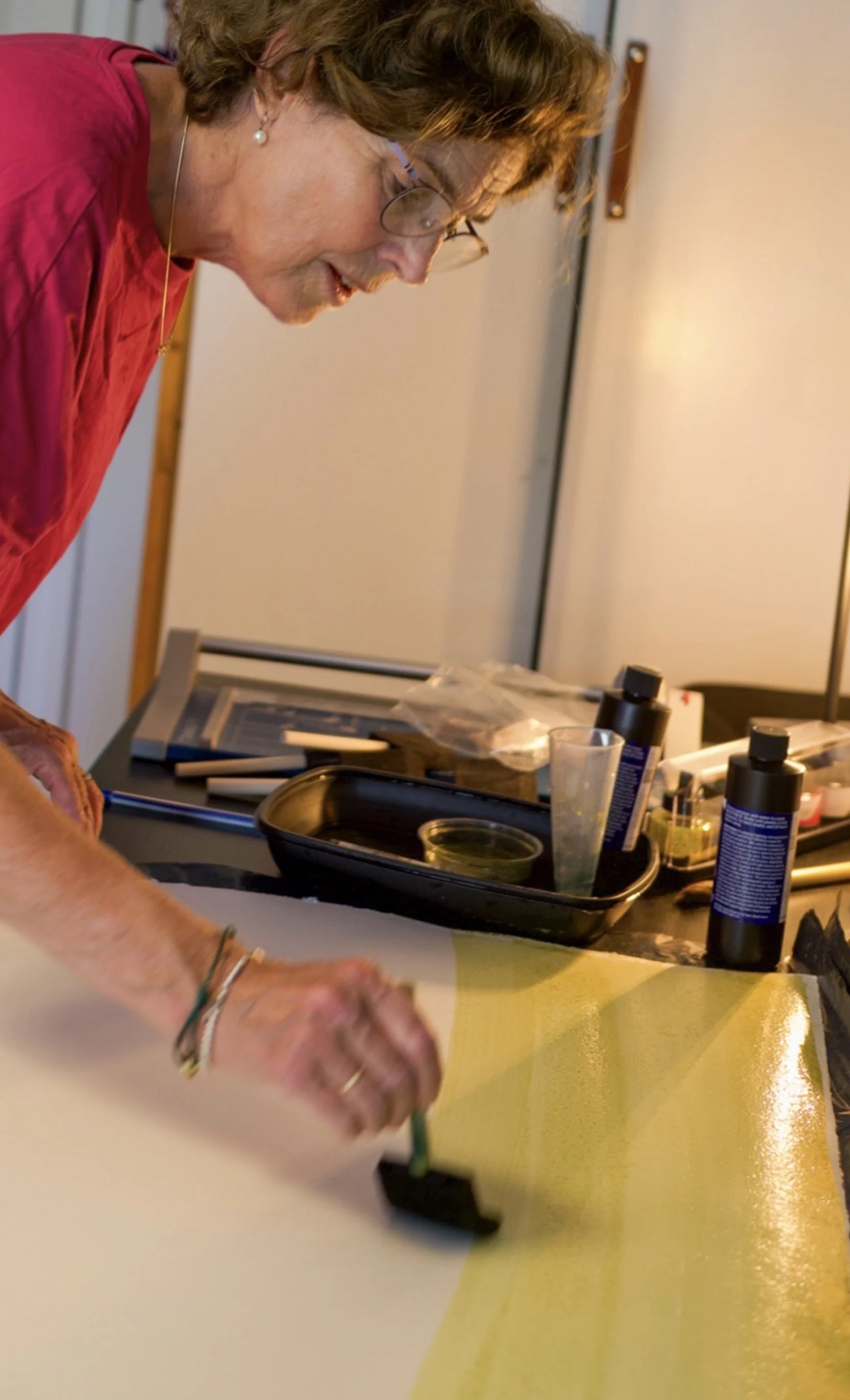 Een vrouw maakt kunst op een grote kartonnen rol, op een tafel met diverse materialen, waaronder verf en potloden.