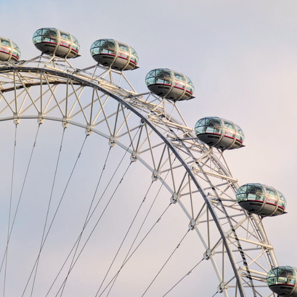 Close-up of a Ferris wheel with glass-enclosed cabins against a cloudy sky.