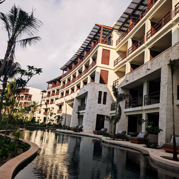 Luxury resort building with multiple balconies and a swimming pool surrounded by tropical plants and palm trees.