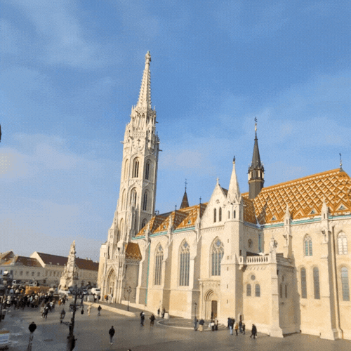 Historical Gothic cathedral with pointed spires and a large clock tower in a busy city square under blue sky.