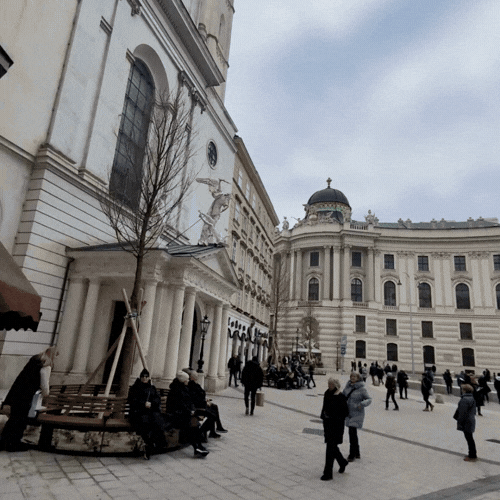 People walking and sitting outside a historic building with classical architecture in an urban area.
