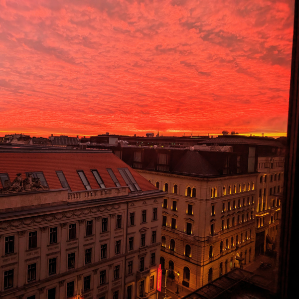 Sunset with bright orange and pink clouds over a cityscape, buildings with lit windows below.