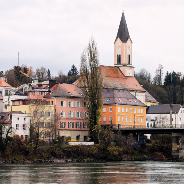 A small European town beside a river with colorful buildings and a church with a tall steeple.