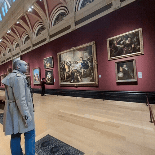 Visitors observing paintings in an art gallery with ornate architectural details.
