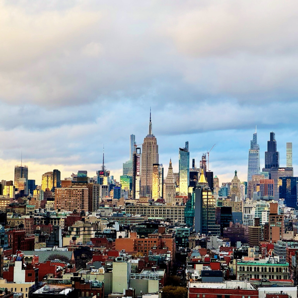 A city skyline of New York City with tall skyscrapers and a cloudy sky.