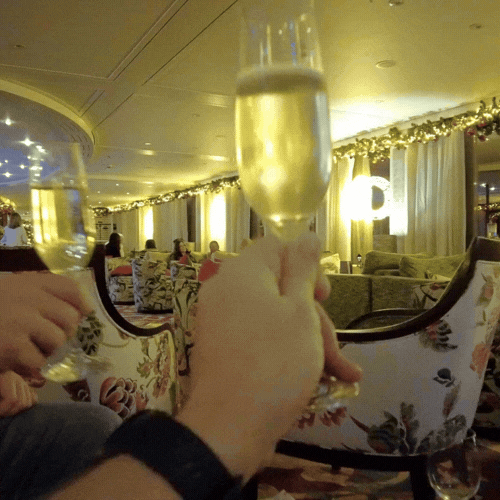 People holding up glasses of champagne in a decorated indoor setting, possibly celebrating a special occasion or enjoying a social gathering.