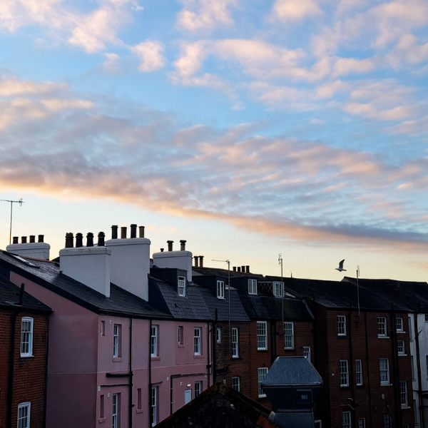 Sky with clouds over a row of residential buildings with chimneys and antennas.