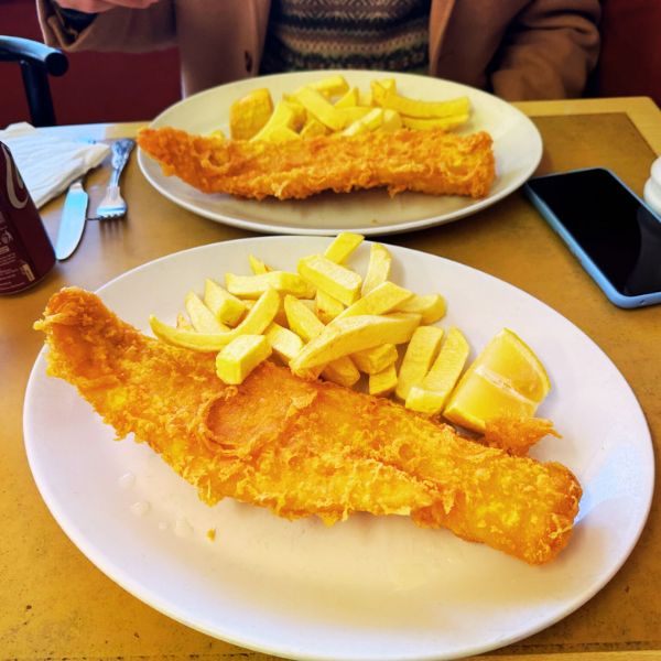 Two white plates with fried fish filets, French fries, and lemon wedges on a restaurant table.