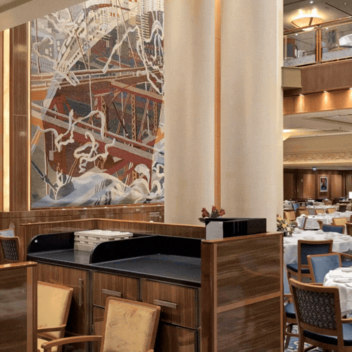 Interior view of a luxurious restaurant with wooden furnishings, white tablecloths, and wall art.