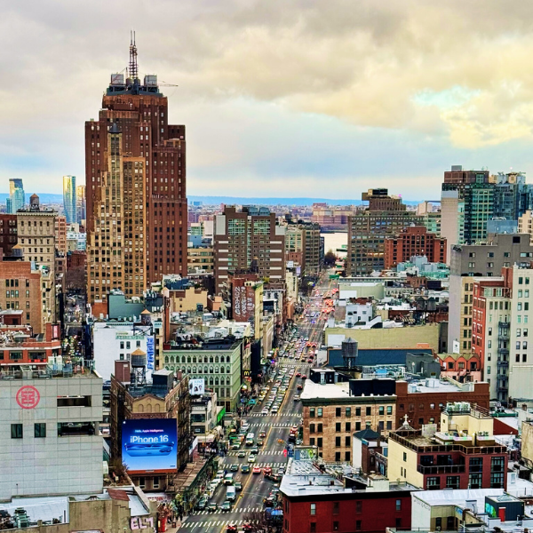 A cityscape view of Manhattan in New York City showing tall buildings, busy streets filled with cars, and a cloudy sky.