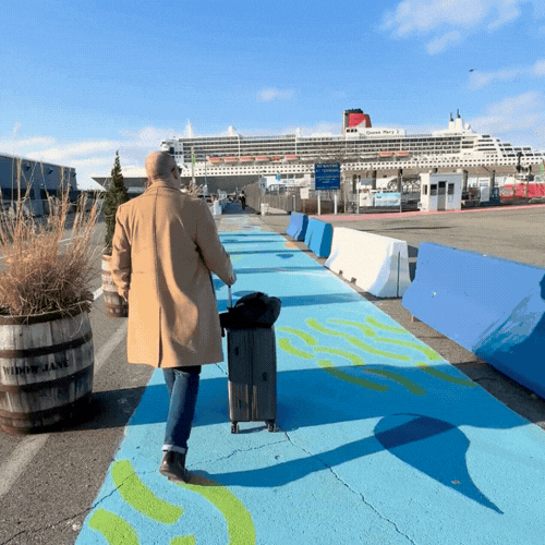 Person walking with rolling suitcase on colorful painted sidewalk near cruise ship