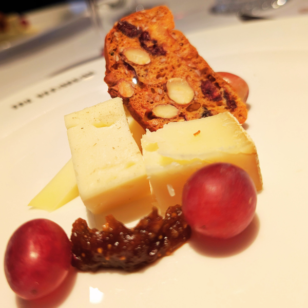 Cheese, grapes, and a biscotti on a white plate.