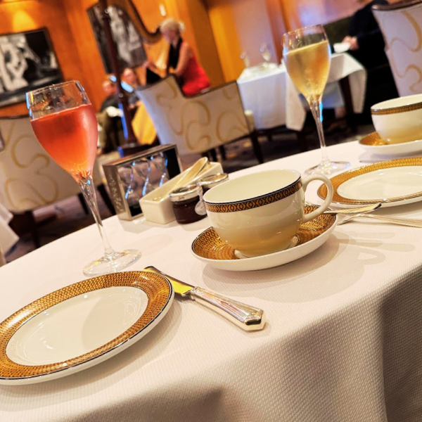 Table setting with plates, cups, glasses with pink and white beverages, cutlery, and condiments in a restaurant with people in the background.