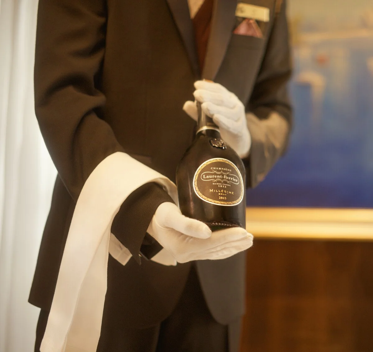 A person dressed in formal attire holding a bottle of Laurent Perrier champagne.
