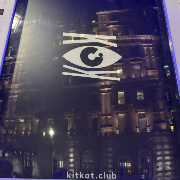 A sign with an eye and lines, reflecting a building's exterior at night, with the website kitkat.club below.