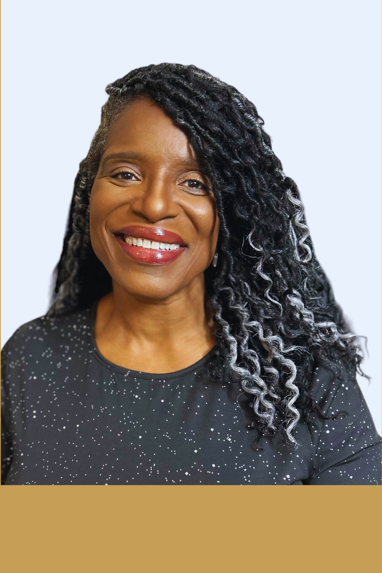 Smiling woman with curly hair and a dark shirt featuring white speckles, against a light background.