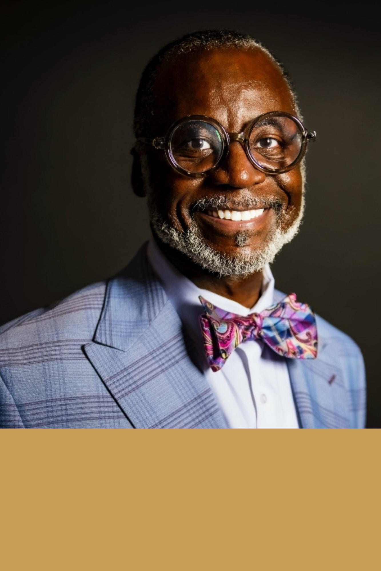 Smiling man with glasses, wearing a plaid suit and colorful bow tie