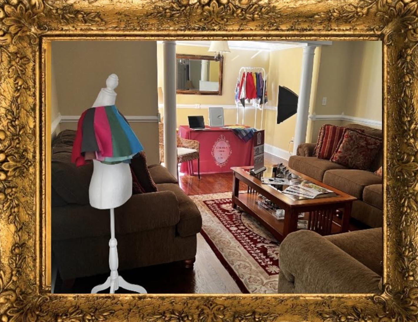 A living room with two brown sofas, a coffee table with magazines, a mannequin covered with colorful fabric, and a pink table with a chair in the background, all enclosed in a gold ornate frame.