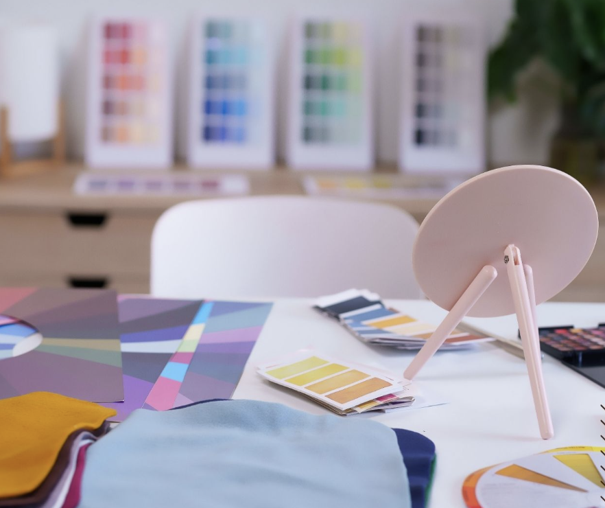 Person holding a color swatch fan deck surrounded by many other color swatches on a wooden surface.