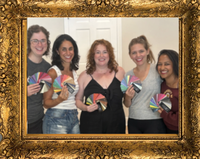 Five women standing indoors, smiling, and each holding a fan deck of color swatches, in front of a white door and wall.