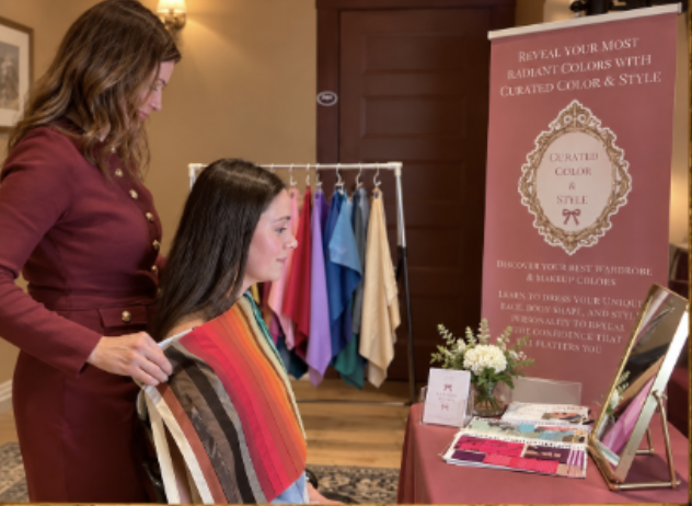 A woman helping a young woman explore fabric and color options at a color consultation exhibit, with fabric swatches on a clothing rack and informational signs in the background.