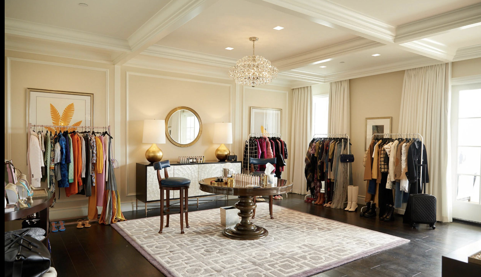 Clothing rack with jackets and sweaters, a beige hat hanging on the side, and tan high heels on a white furry rug on a concrete floor