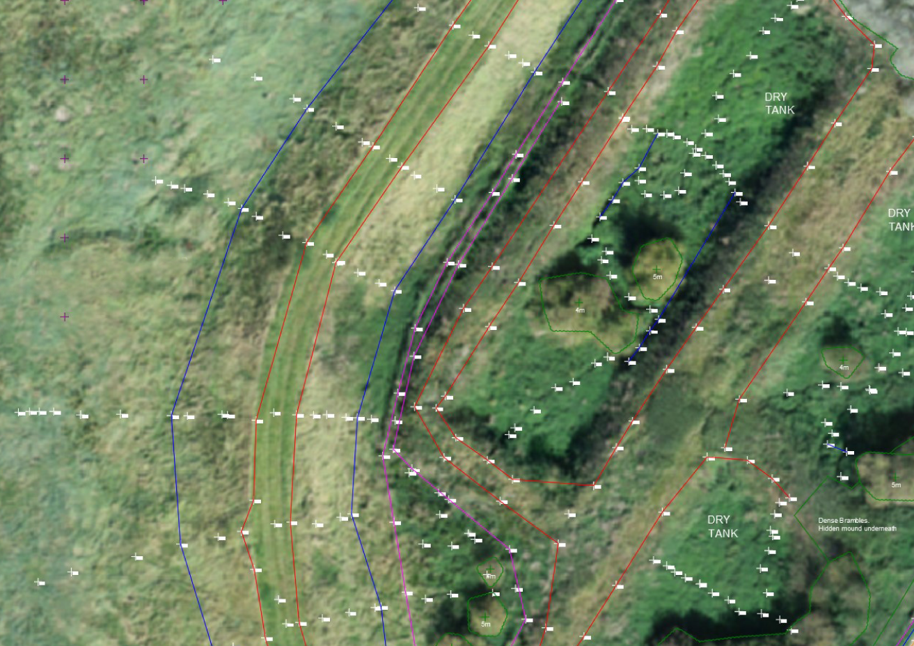 An aerial view of farmland showing areas marked with red and blue lines, and labels indicating dry tanks, dense brambles, and hidden mounds underneath. The terrain is green with some darker patches of vegetation.