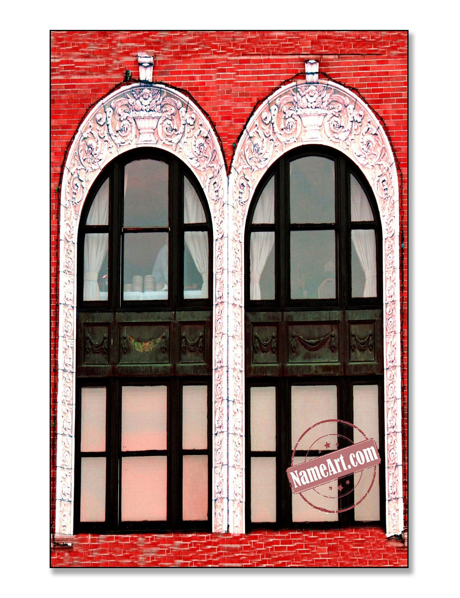 Two large arched windows with ornate white trim on a red brick building, with curtains and dishes visible through the windows.