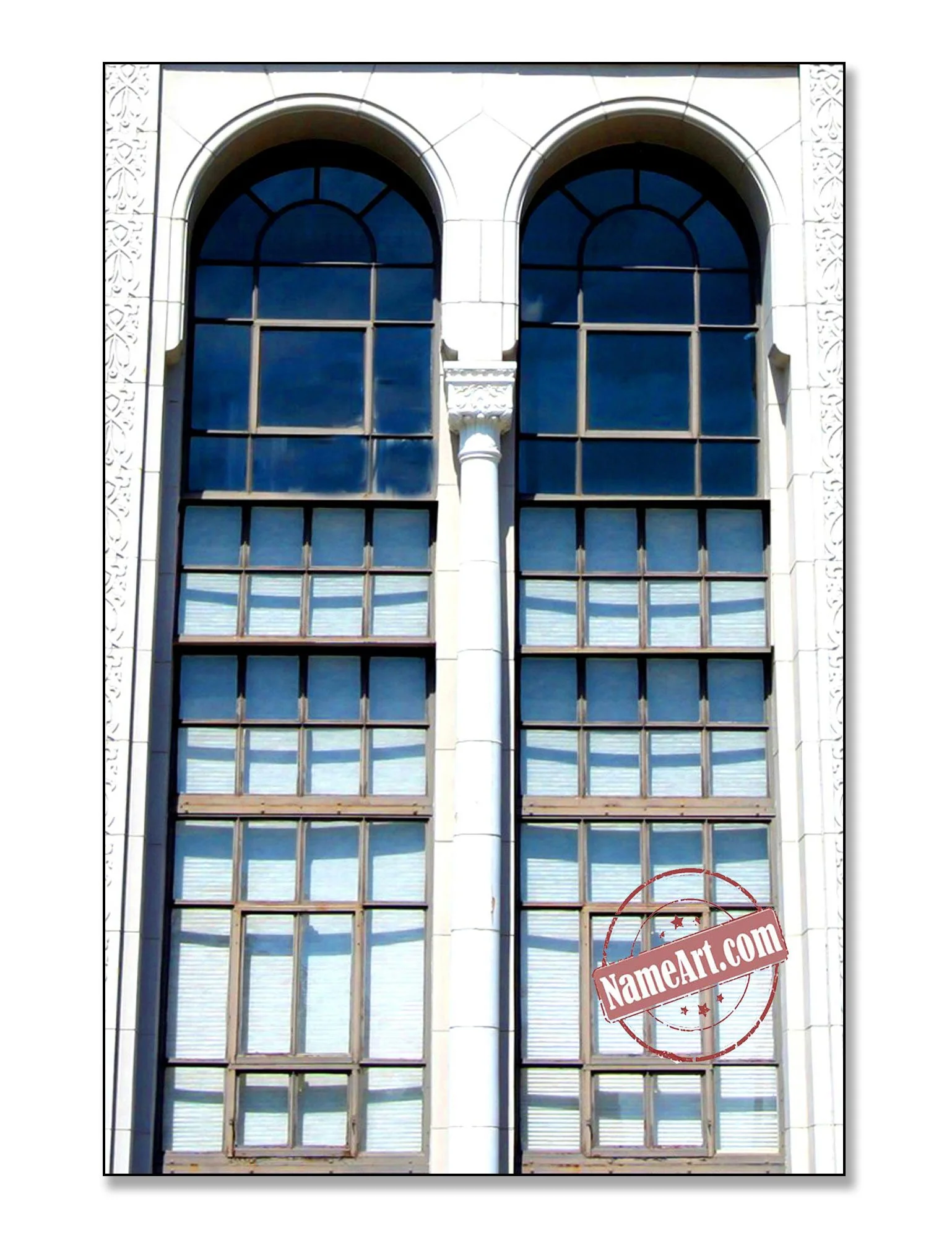 Close-up of a building facade with large arched windows reflecting blue sky and clouds, framed by ornate white stone, with a column and a stamp watermark reading 'NameArt.com'.
