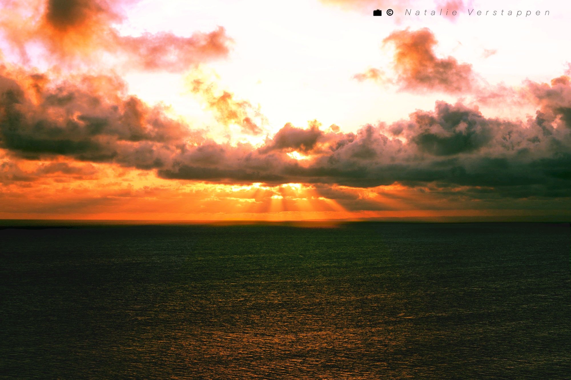 Clouds diffusing the light of the sun going down over the ocean