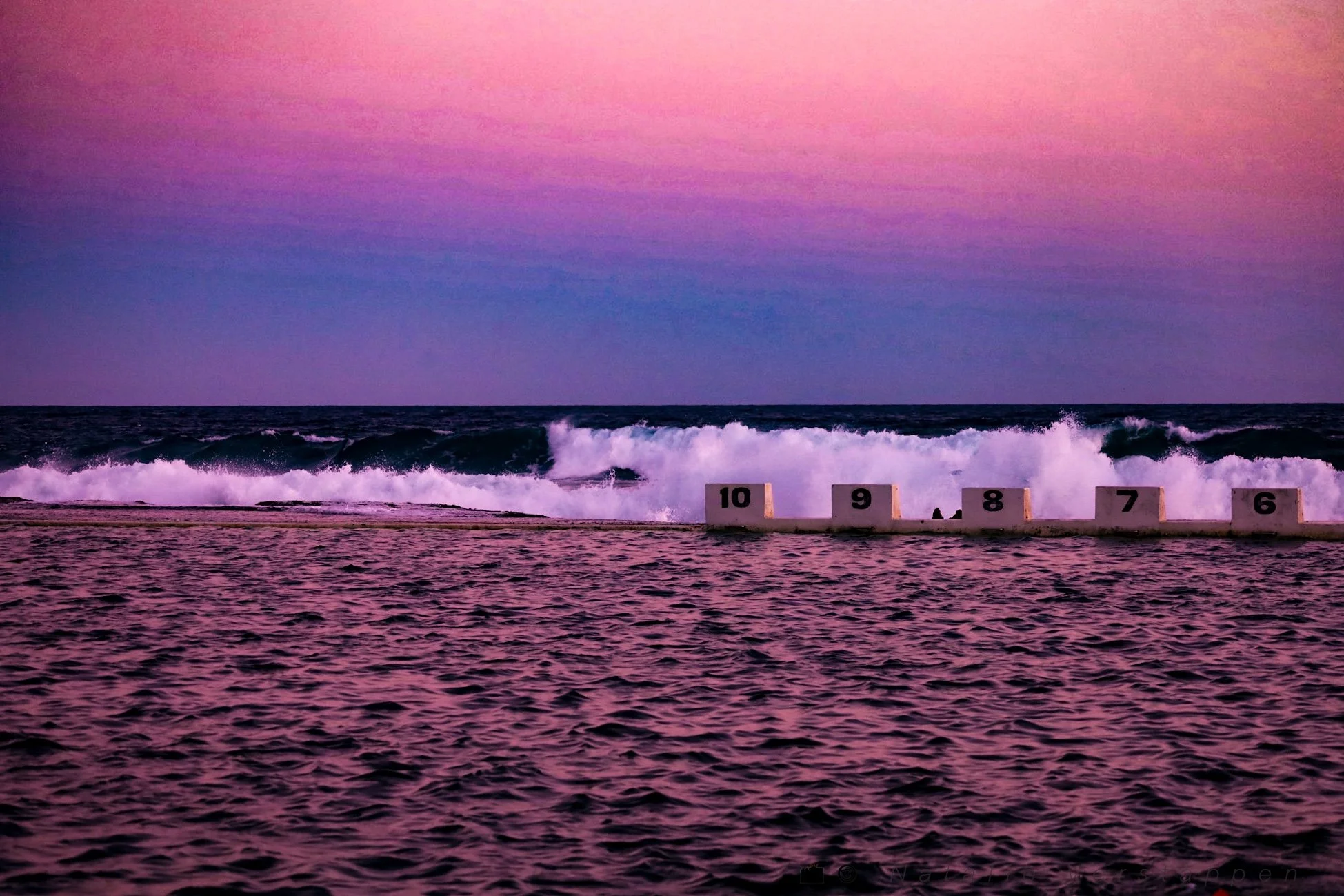 Waves crashing into a natural pool with blue and pinks shades in the sky