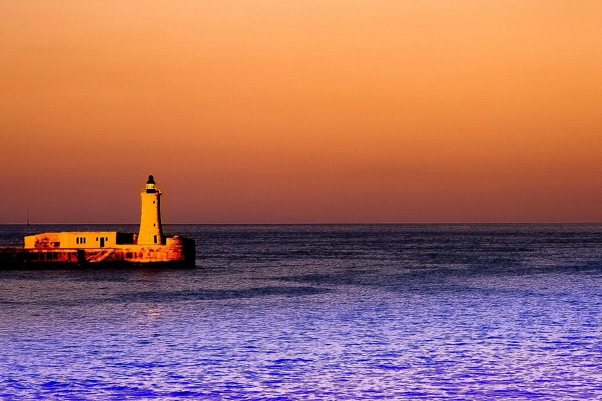 Lighthouse on the end of the harbour, in a haze of golden hour light