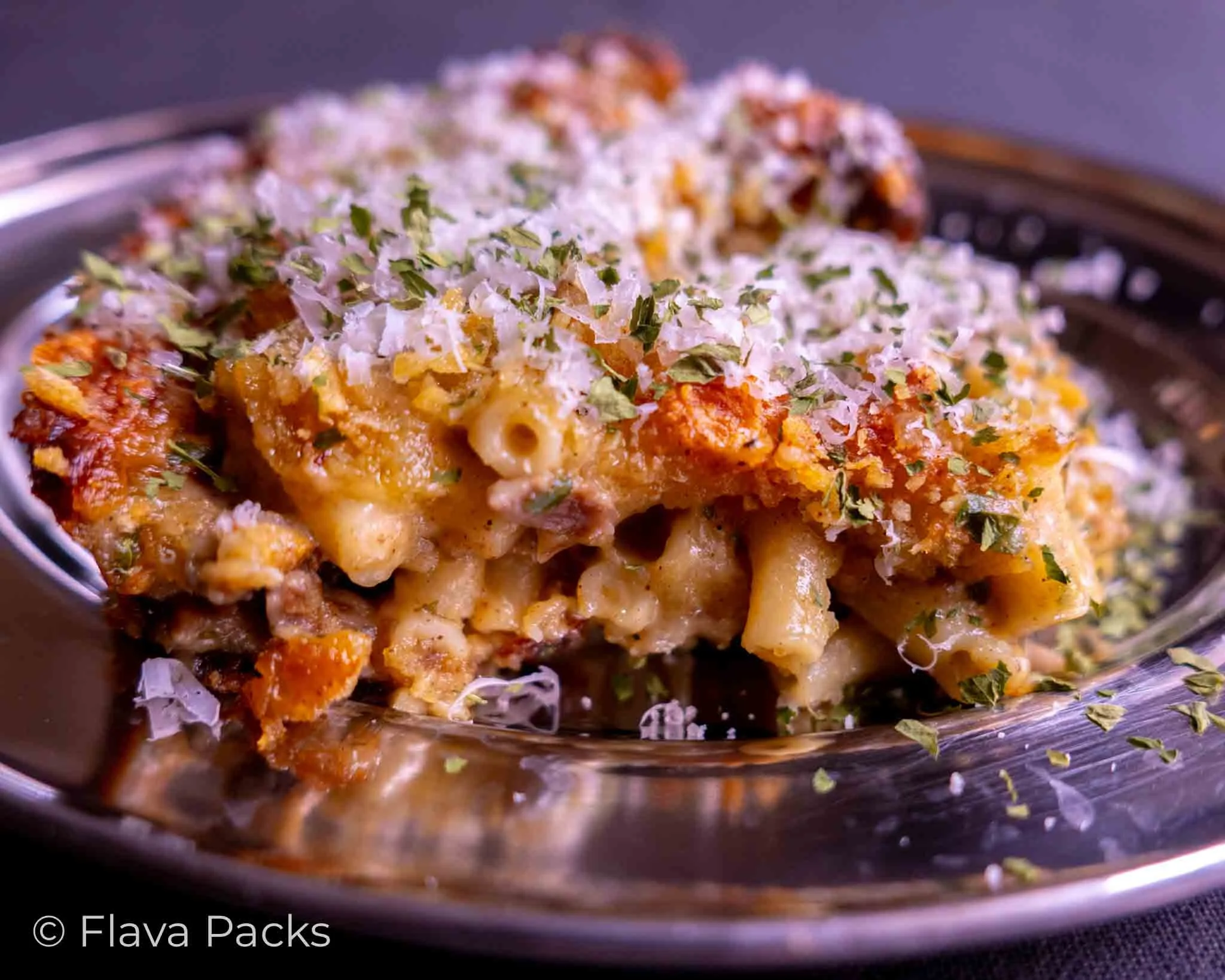 Jerk Lamb Mac & Cheese topped with parmesan on a stainless steel dish