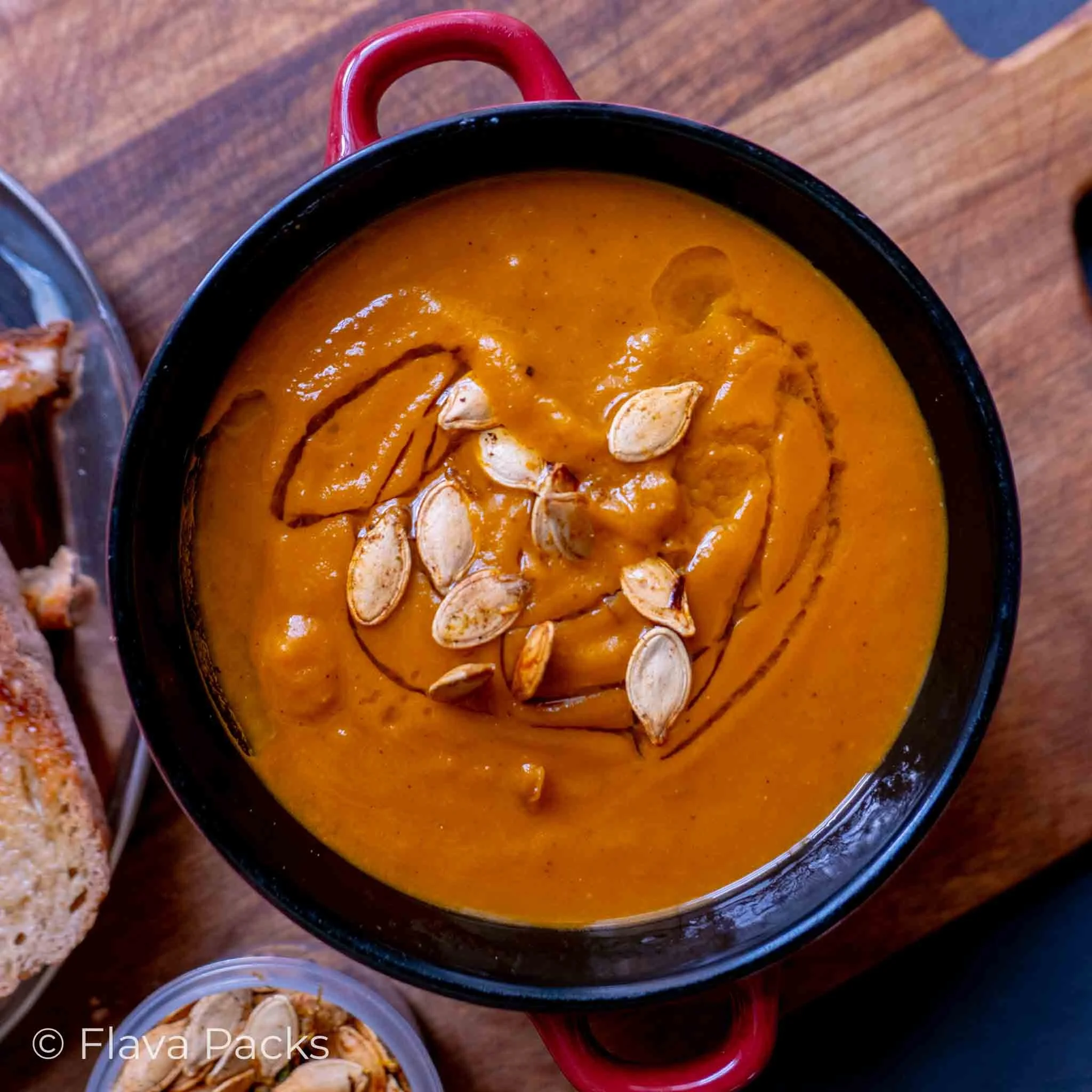 A Jerk Spicy Pumpkin Soup topped with roasted pumpkin seeds and extra virgin olive oil in a bowl on a wooden chopping board