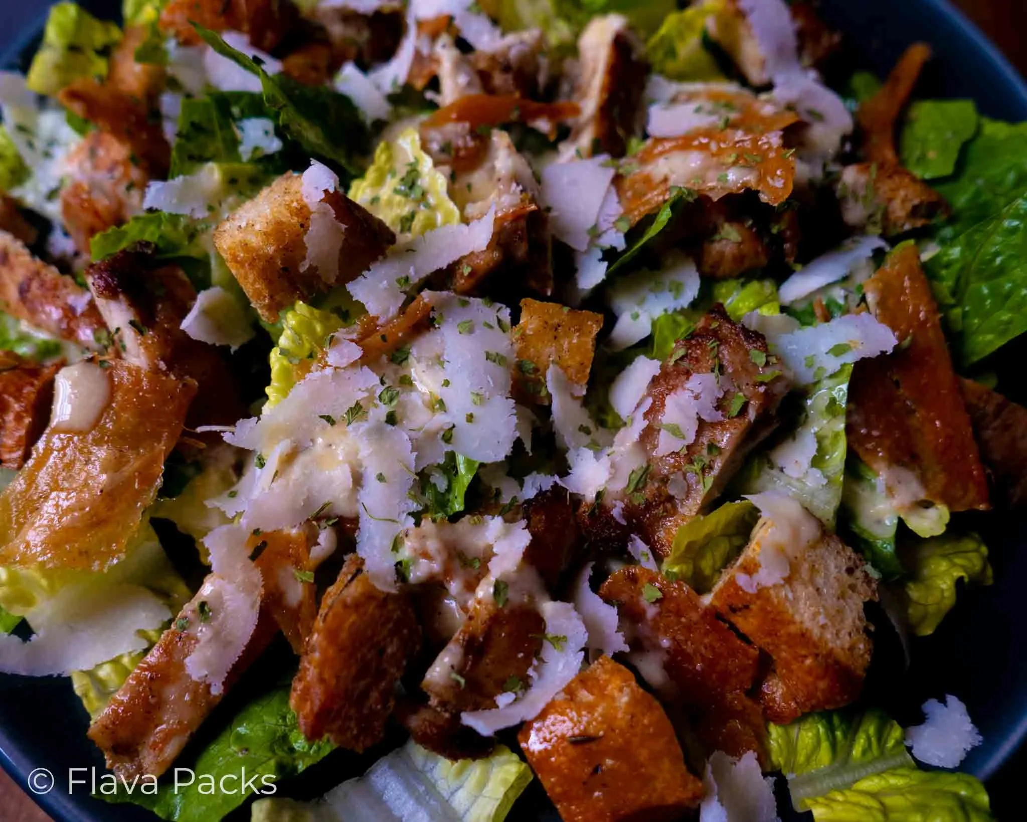 Close up on a Jerk Chicken Caesar salad made with croutons, cos lettuce, parmesan shavings, grilled jerk chicken and caesar dressing