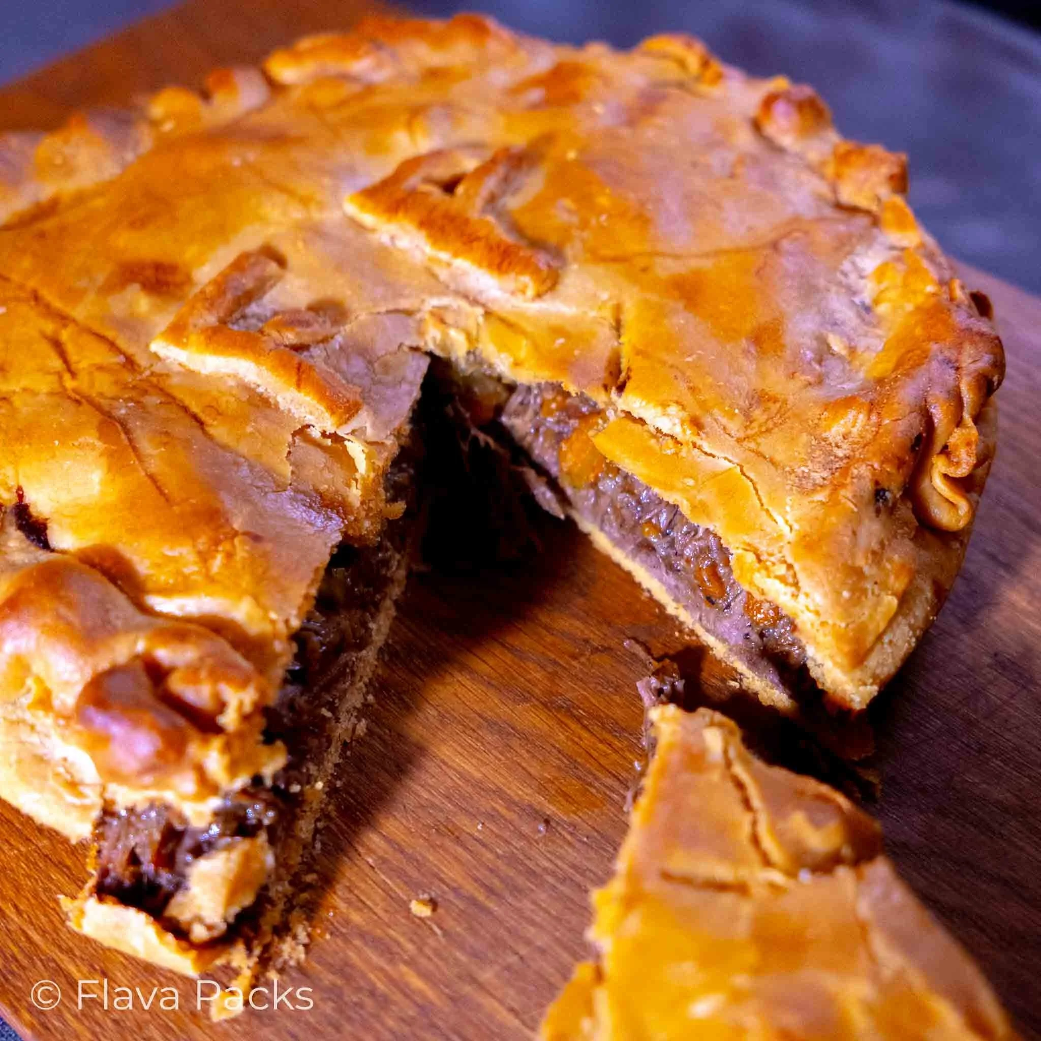 A Jerk Beef Short Rib Pie with a slice cut out, sitting on a wooden chopping board.