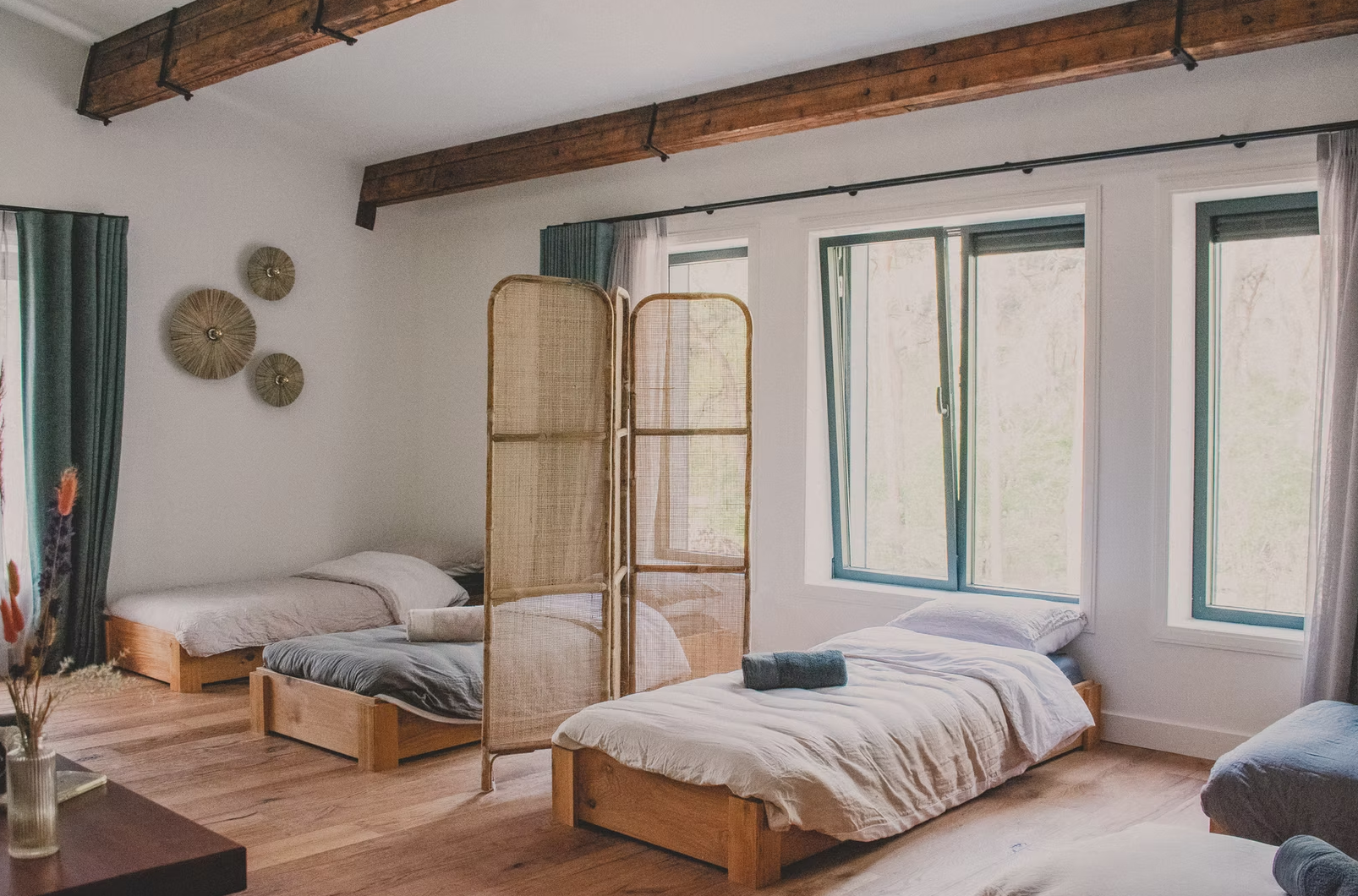 A bedroom with three single beds, a folding room divider, large windows, and wall decorations.