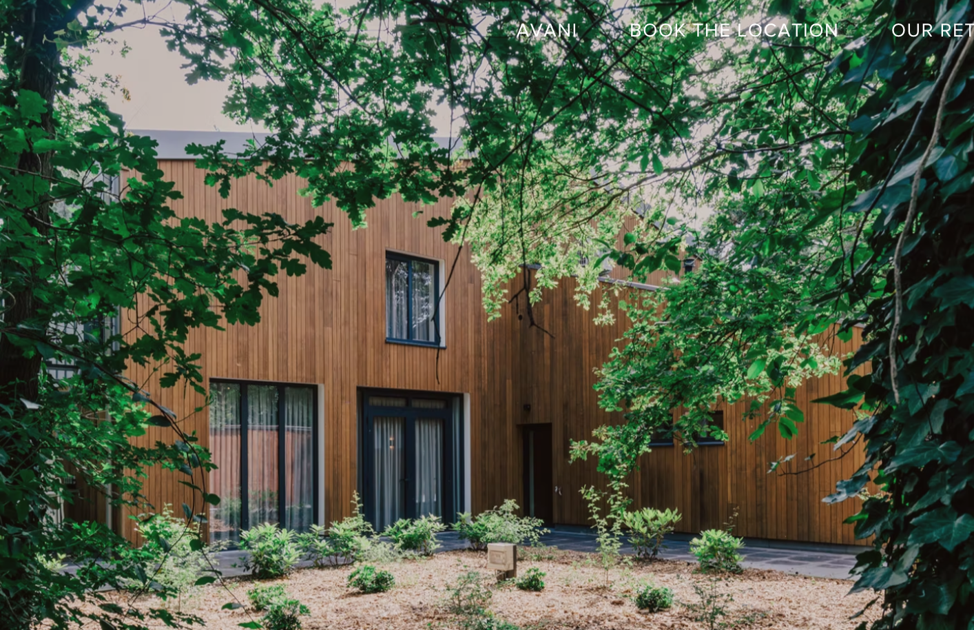 Modern wooden house with large windows, surrounded by greenery and trees.