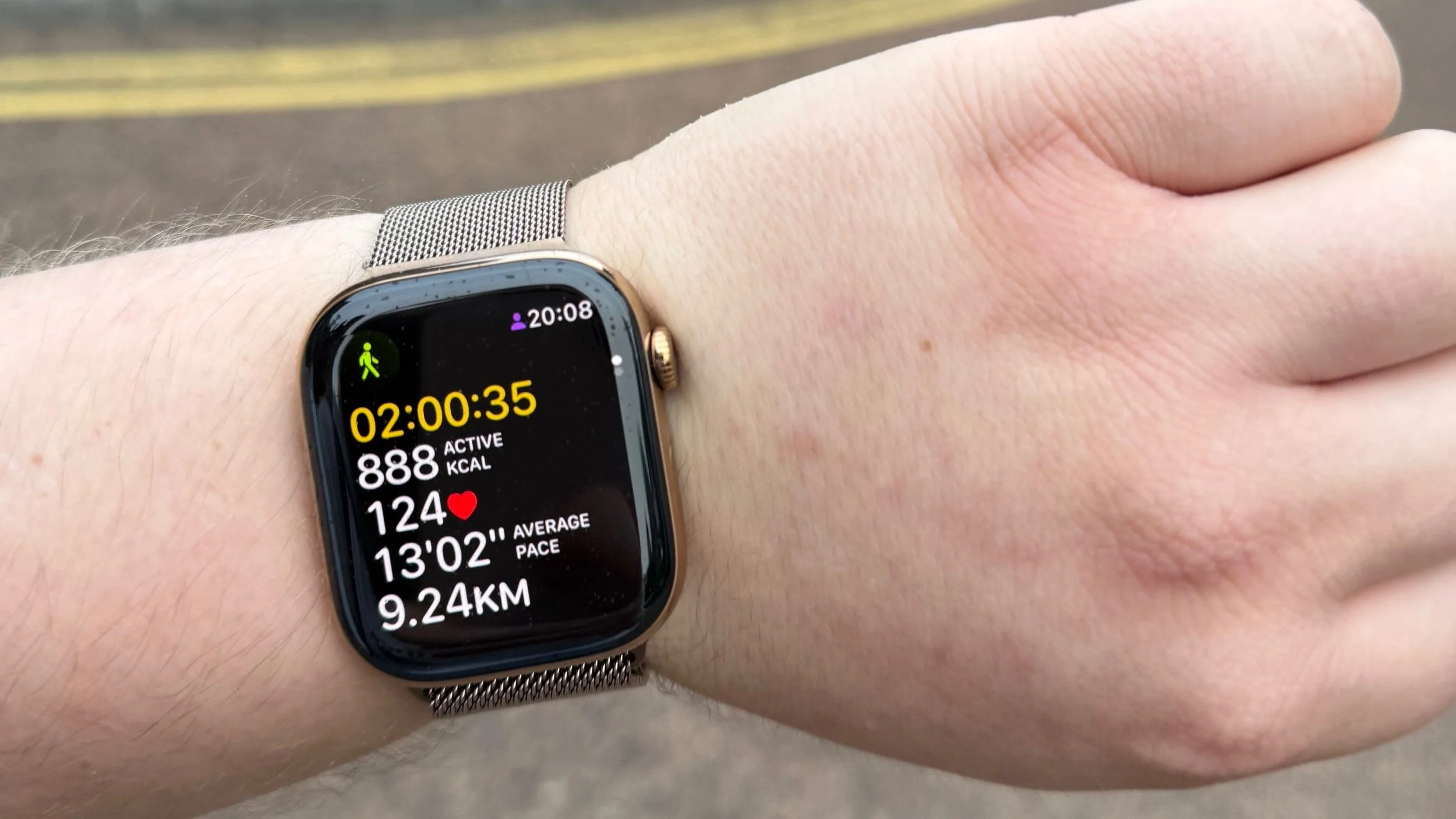 Photo of an Apple Watch showing the workout screen tracking a walk, the watch is on my left arm, with road visible in the background. The watch shows a time of 2 hours and over 9km tracked