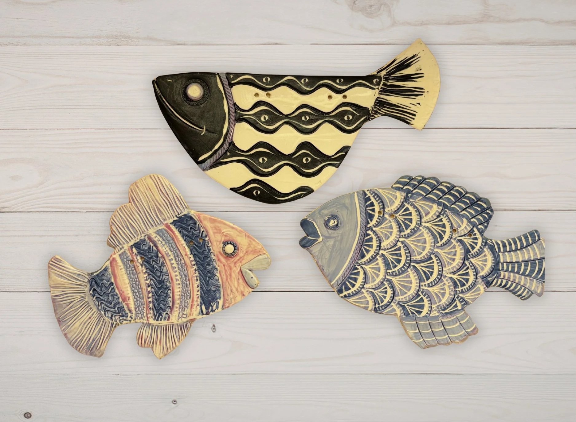 three clay wall hanging fish of varying shapes and colors