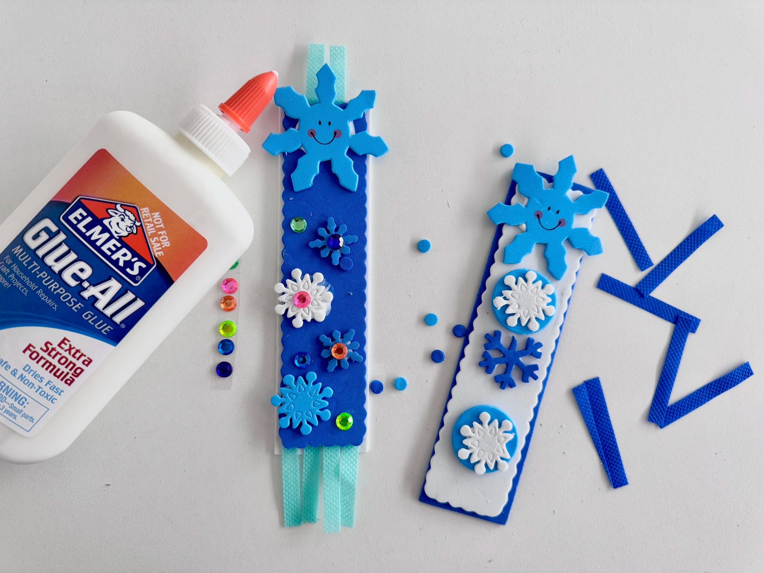 blue and white snowflake bookmarks with gem stickers next to a bottle of elmer's glue
