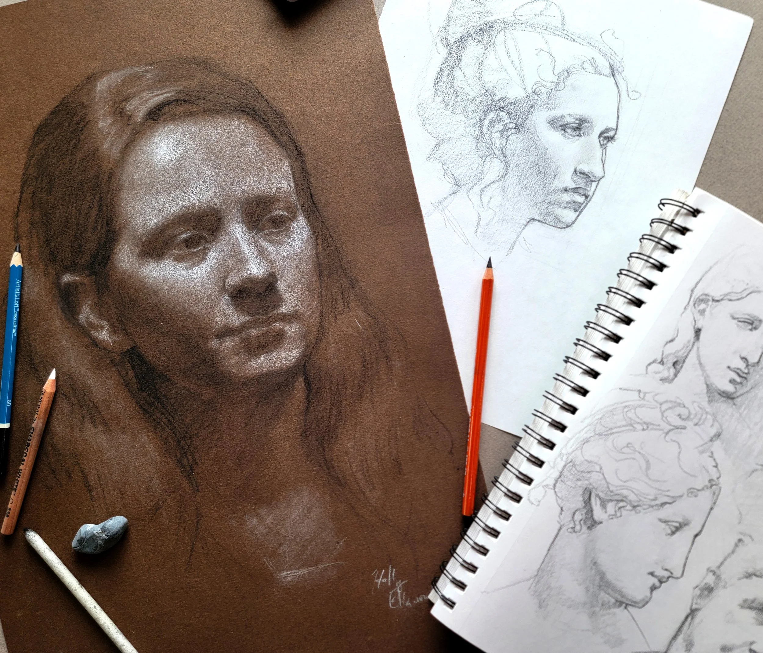 a drawing of a face next to sketches in a notebook and pencils