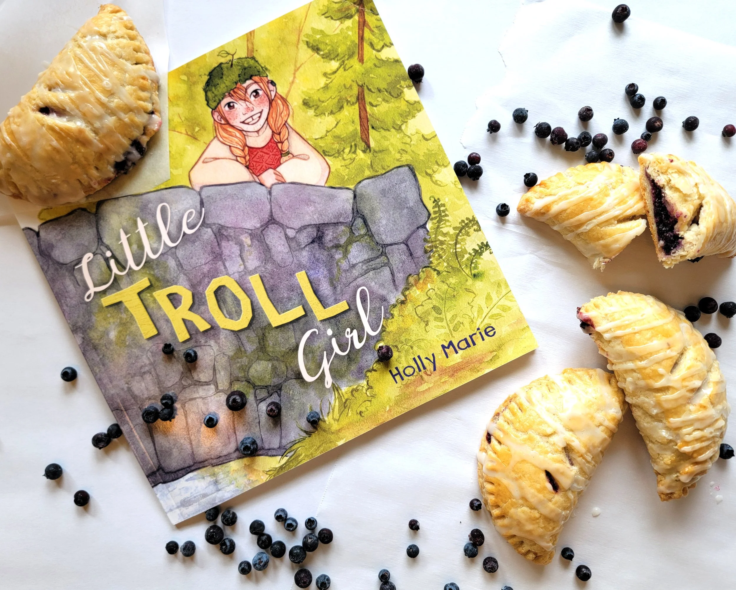 the book The Little Troll Girl surrounded by blueberries and blueberry hand pies