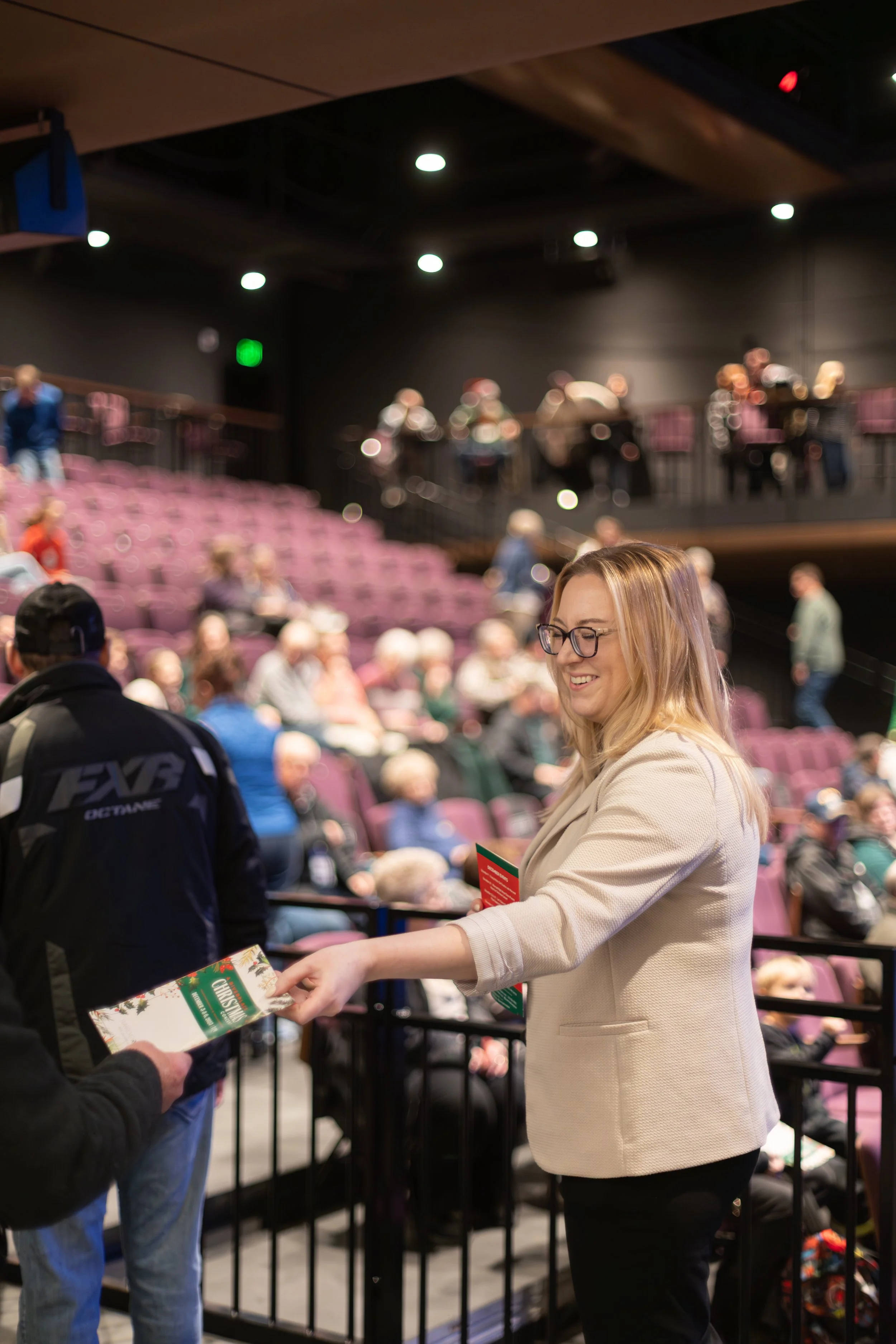 Executive Director Samantha Harrill handing out Christmas concert programs at the door of the RiverPlace performance hall