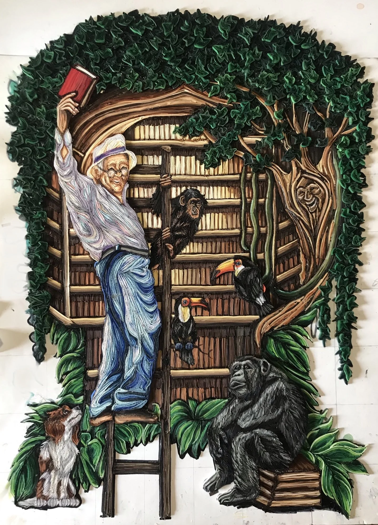 Paper quilling piece, "The Great Discovery...Patrick - The Librarian," by Nikki Besser, featuring a man holding a book by a wall full of books surrounded by nature like chimps and birds