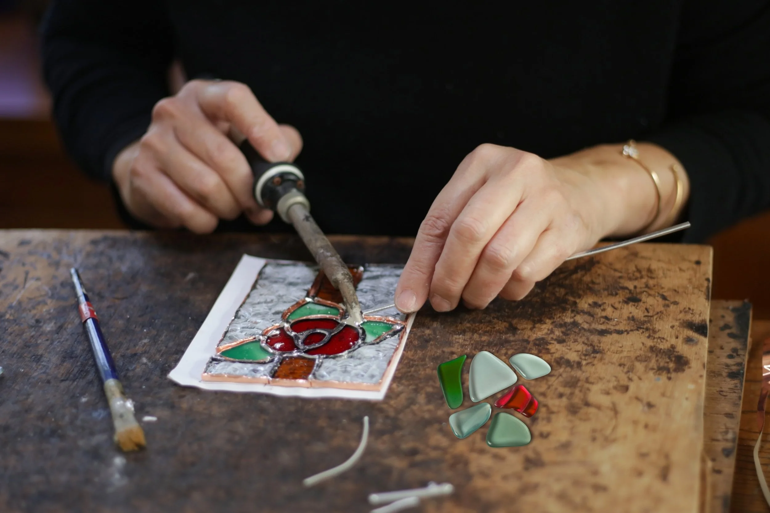 an upclose shot of someone's hands using a soldering iron to make a stained glass object with a red rose