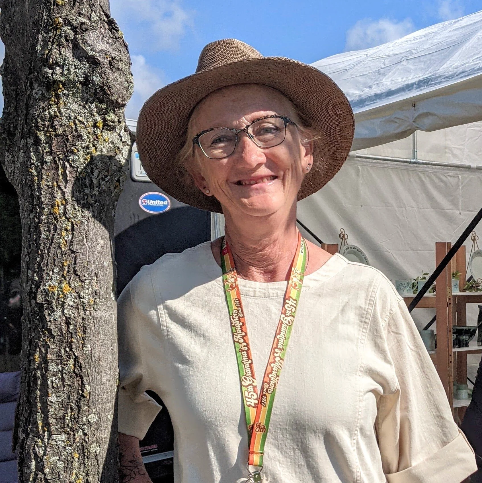 a photo of potter Betsy Saurdiff standing next to a tree and wearing a hat in the summer